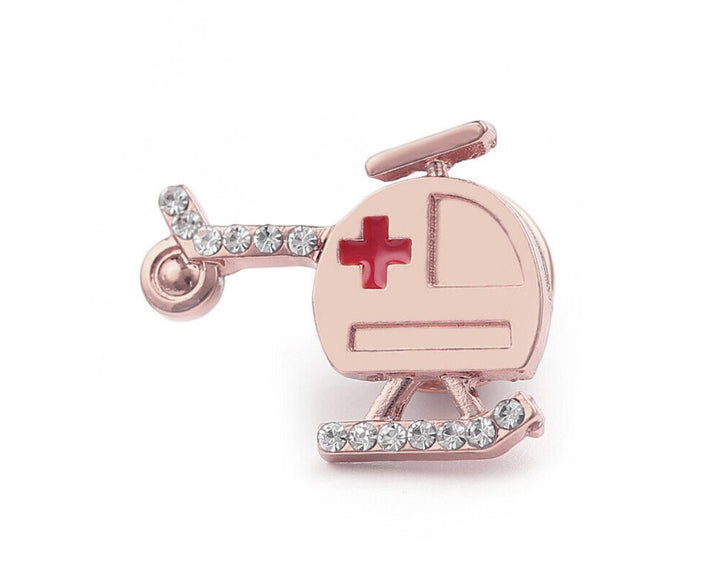 A rose gold pin shaped like an air ambulance helicopter, adorned with sparkling rhinestones and featuring a red cross symbol, making it a perfect accessory for medical professionals such as doctors, nurses, and paramedics