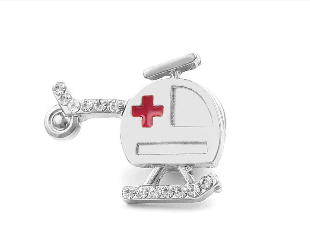 A silver air ambulance lapel pin brooch shaped like a helicopter, featuring a red cross symbol and embellished with sparkling rhinestones, ideal for medical professionals such as doctors, nurses, and paramedics.