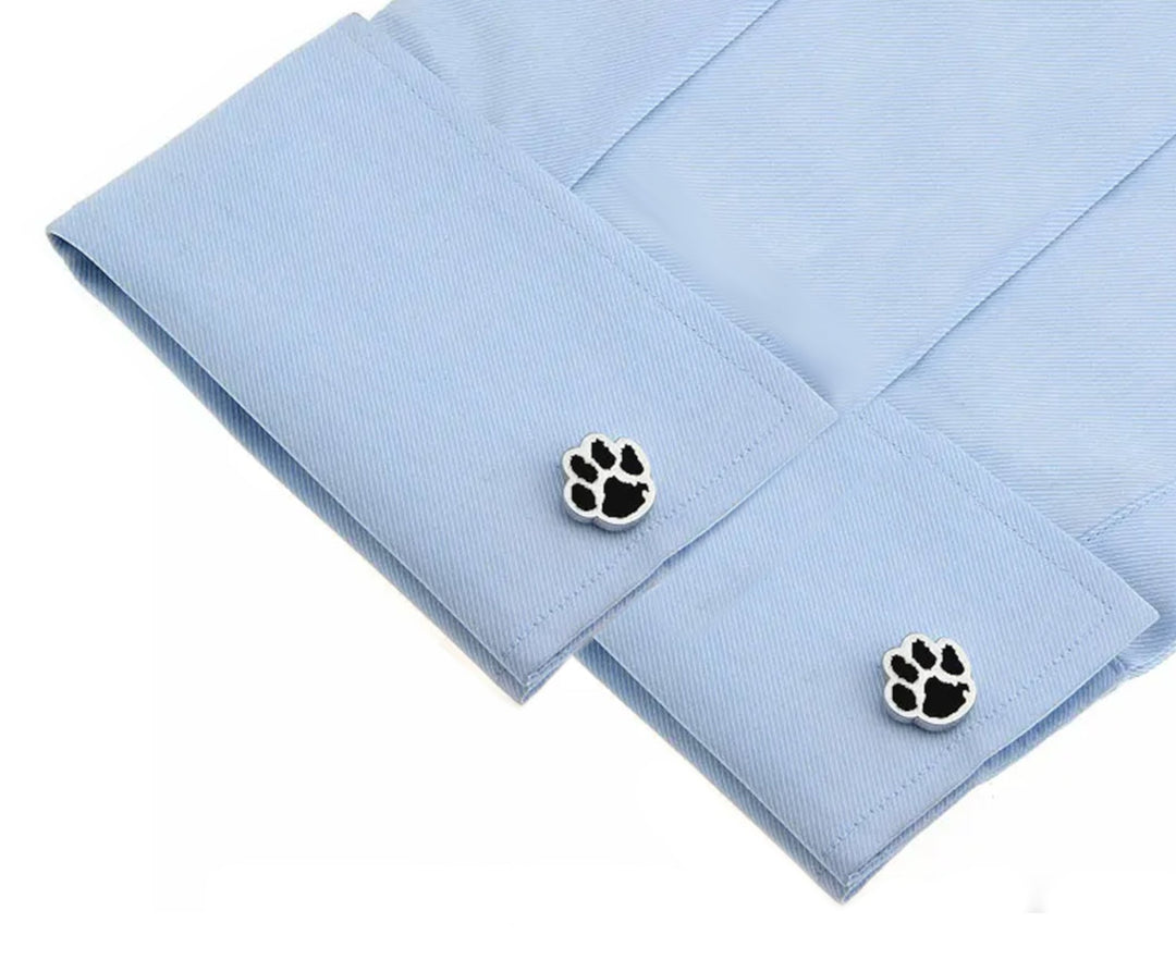 Paw shaped silver coloured cufflinks with black enamel insets displayed on the cuffs of a blue shirt