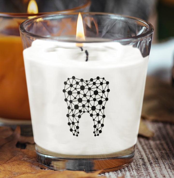 A scented candle featuring an abstract tooth design on the label, set against a soft background, perfect for dental professionals or as a unique gift.