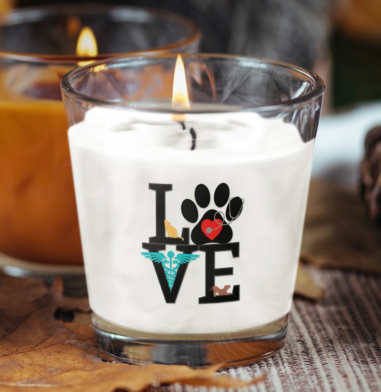 Decorative candle in a glass holder featuring the word 'LOVE' with a paw print, a heart, and a veterinary symbol, symbolizing the bond between pets and their caregivers.